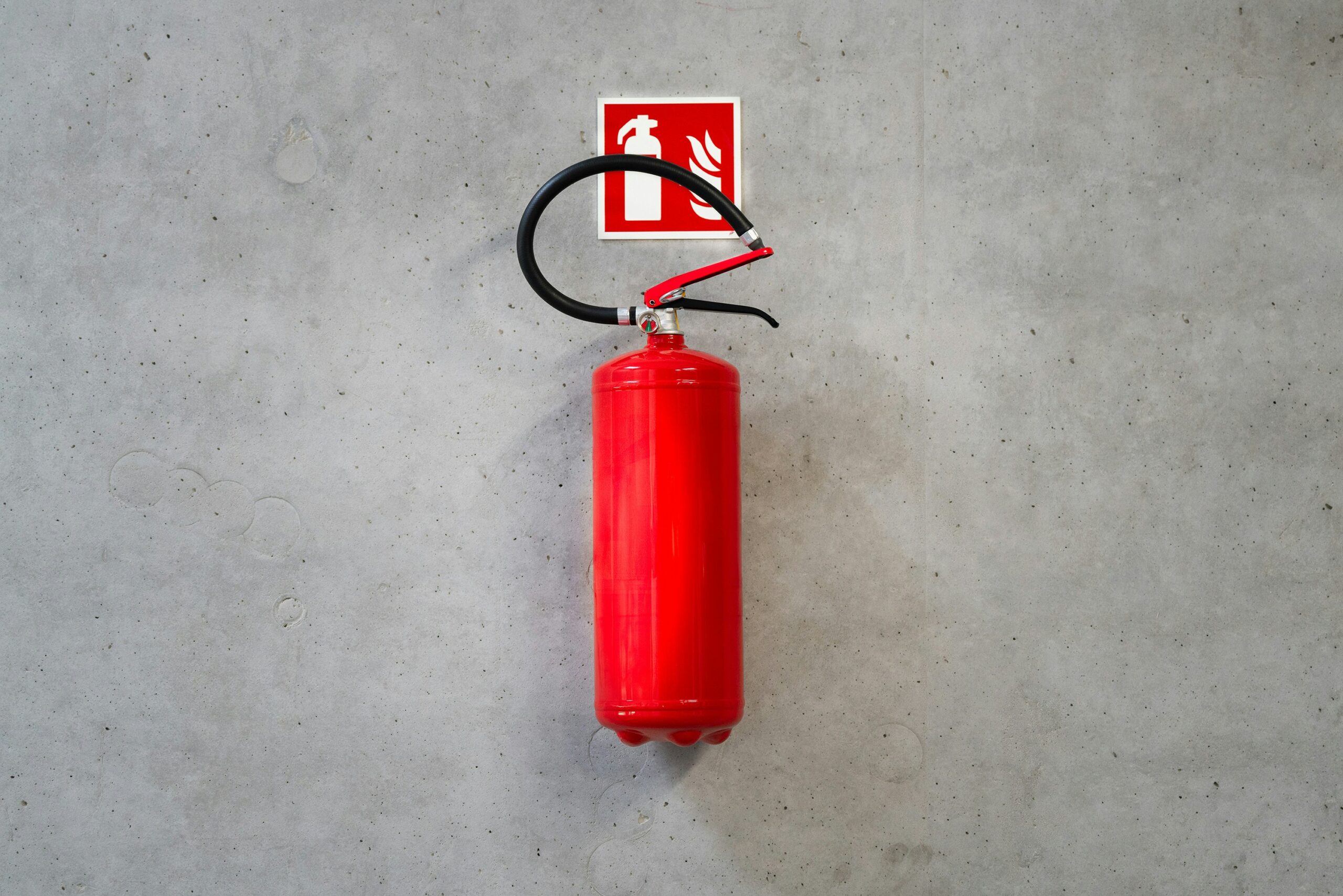 Extintor de incendios reglamentario instalado sobre una pared con señalización de fondo rojo en una empresa.
