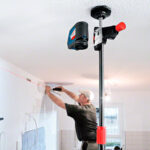Operario trabajando en el montaje de una salida de aire en la pared utilizando la barra telescópica Bosch BT 350 ajustada al techo.