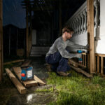 Operario trabajando en el exterior bajo la lluvia con la linterna Bosch GLI 18V-1500 iluminando la zona desde el suelo.