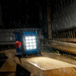 Linterna Bosch GLI 18V-1500 encendida bajo la lluvia sobre vigas de madera demostrando su resistencia IP64.