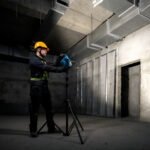 Técnico instalando la linterna Bosch PRO GLI 18V-3000 sobre un trípode de obra en una habitación en construcción.