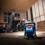 Vista trasera de la linterna Bosch PRO GLI 18V-3000 apoyada en el suelo iluminando un taller de carpintería.