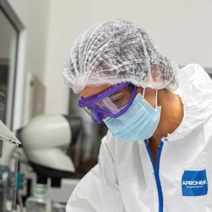 Profesional en laboratorio utilizando antiparra de protección ocular transparente, barbijo y traje de protección biológica.