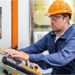 Operario industrial trabajando con casco naranja, gafas de protección y tapones auditivos Libus Quantum colocados con cordón azul.
