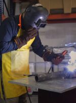 Operario de soldadura realizando trabajos sobre estructura metálica con el delantal de cuero descarne reforzado.