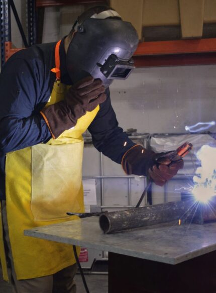Operario de soldadura realizando trabajos sobre estructura metálica con el delantal de cuero descarne reforzado.