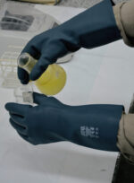 Operario de laboratorio manipulando un matraz de vidrio con líquidos químicos usando los guantes DP DPS91494.