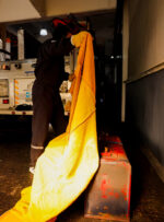 Operario/bombero manipulando la manta ignífuga de descarne de 2 x 2,5 metros para sofocar un contenedor de fuego.