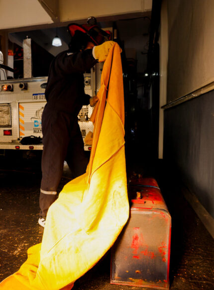 Operario/bombero manipulando la manta ignífuga de descarne de 2 x 2,5 metros para sofocar un contenedor de fuego.